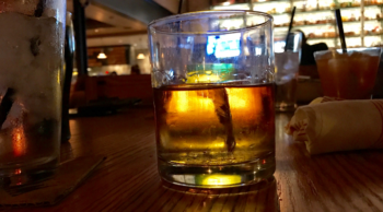 A glass of whiskey on a table backlit by a bar prior to a DWI