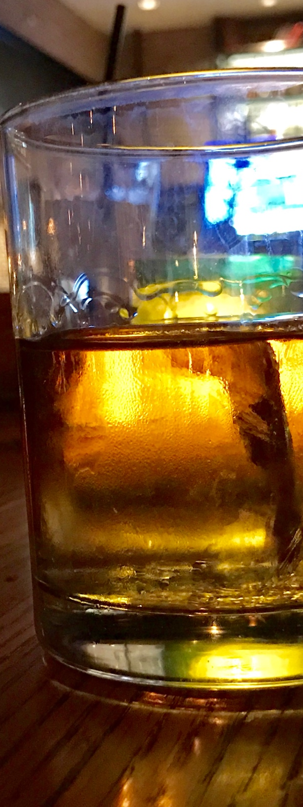 A glass of whiskey on a table backlit by a bar prior to a DWI